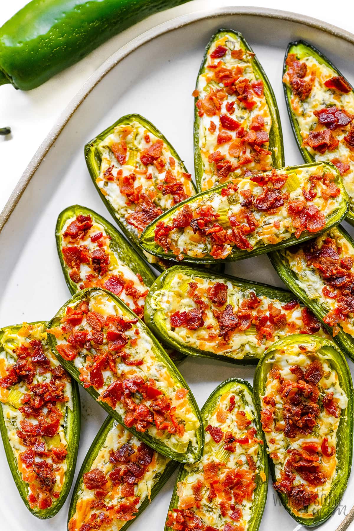 Jalapeno poppers stacked together on a serving platter.