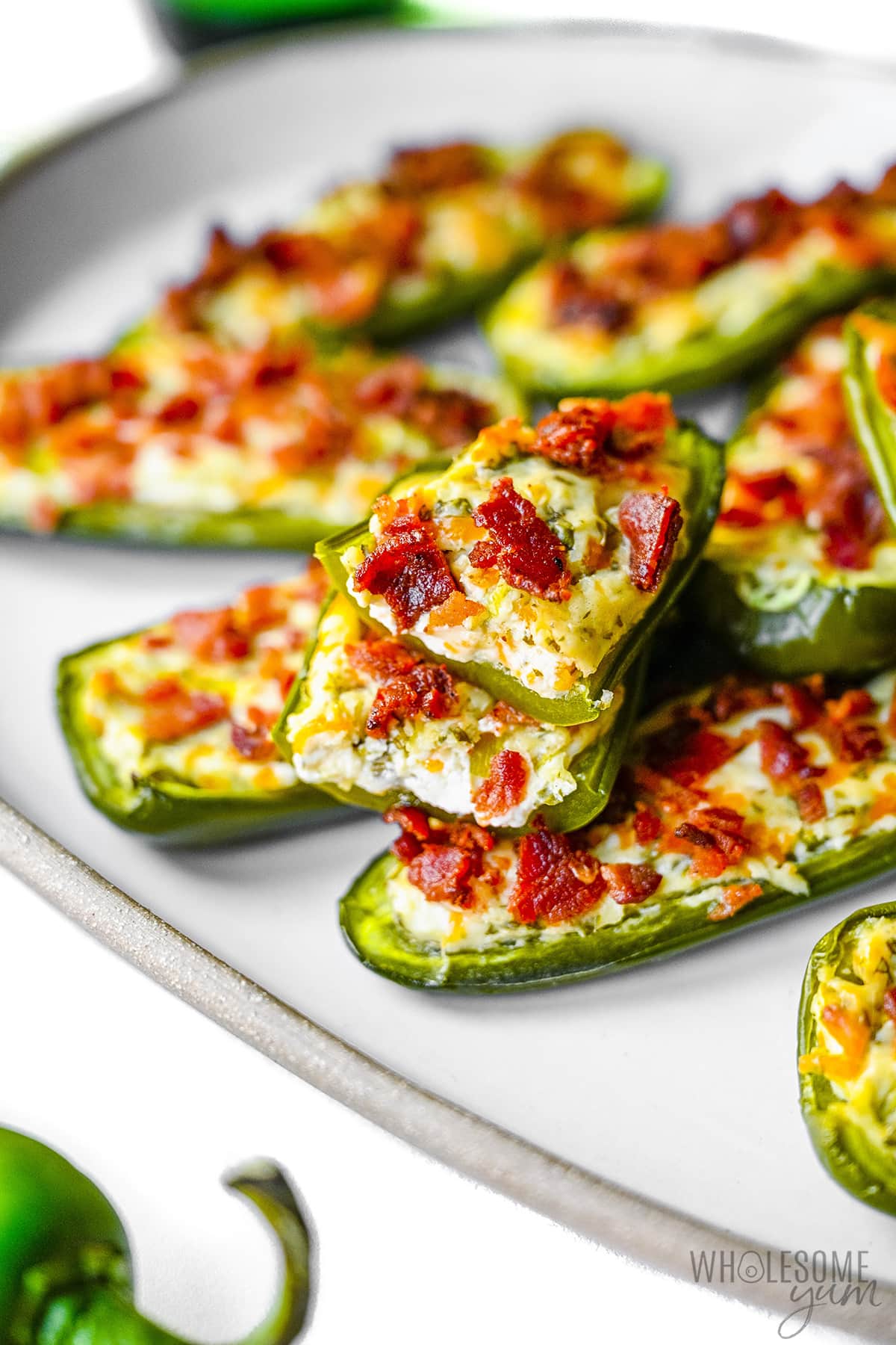 Bacon cream cheese jalapeno poppers on a plate with one split in half.