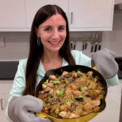 Maya holding a skillet with kelp noodles, juicy chicken, and crisp veggies.