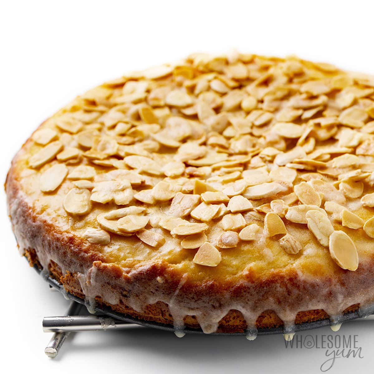 Almond flour cake on cooling rack with toasted almond topping and glaze on top.