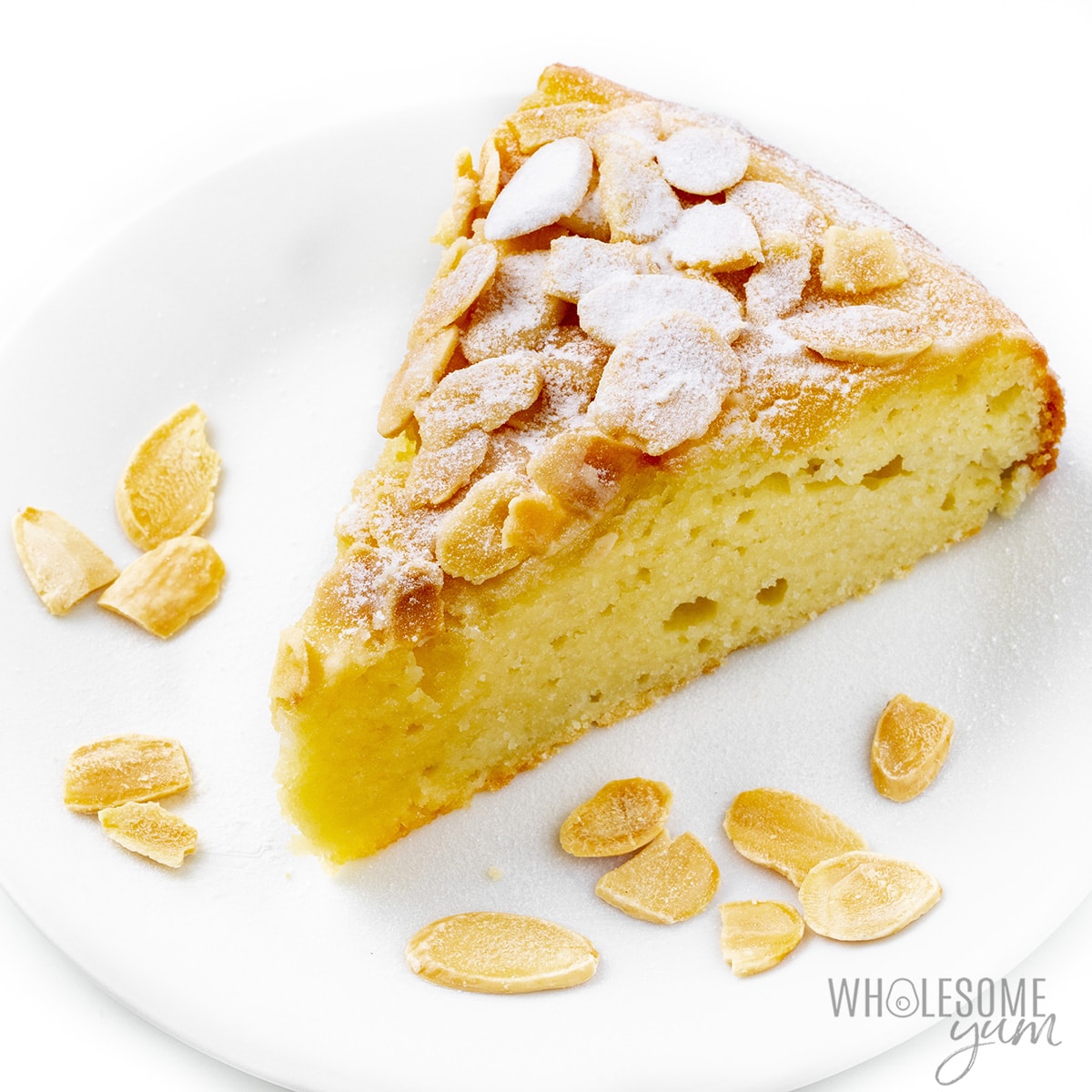 Almond flour cake slice on a plate with almonds.