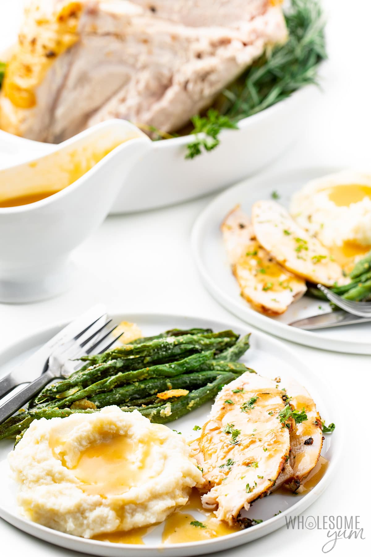Two plates of turkey slices with mashed potatoes and green beans with a carved Crock Pot turkey breast in the background.