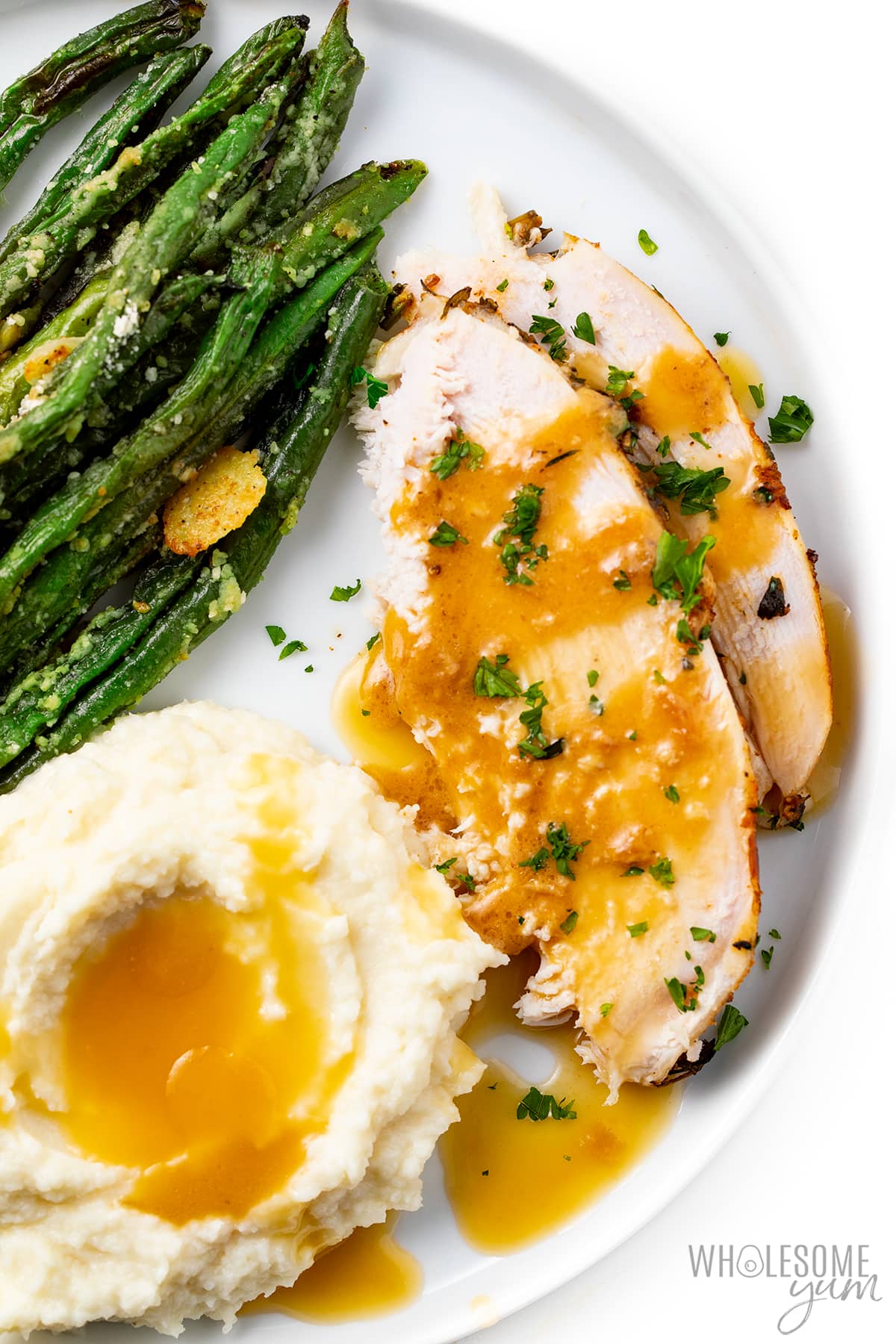Thinly sliced ​​slow cooker turkey breast with gravy, mashed potatoes and green beans.