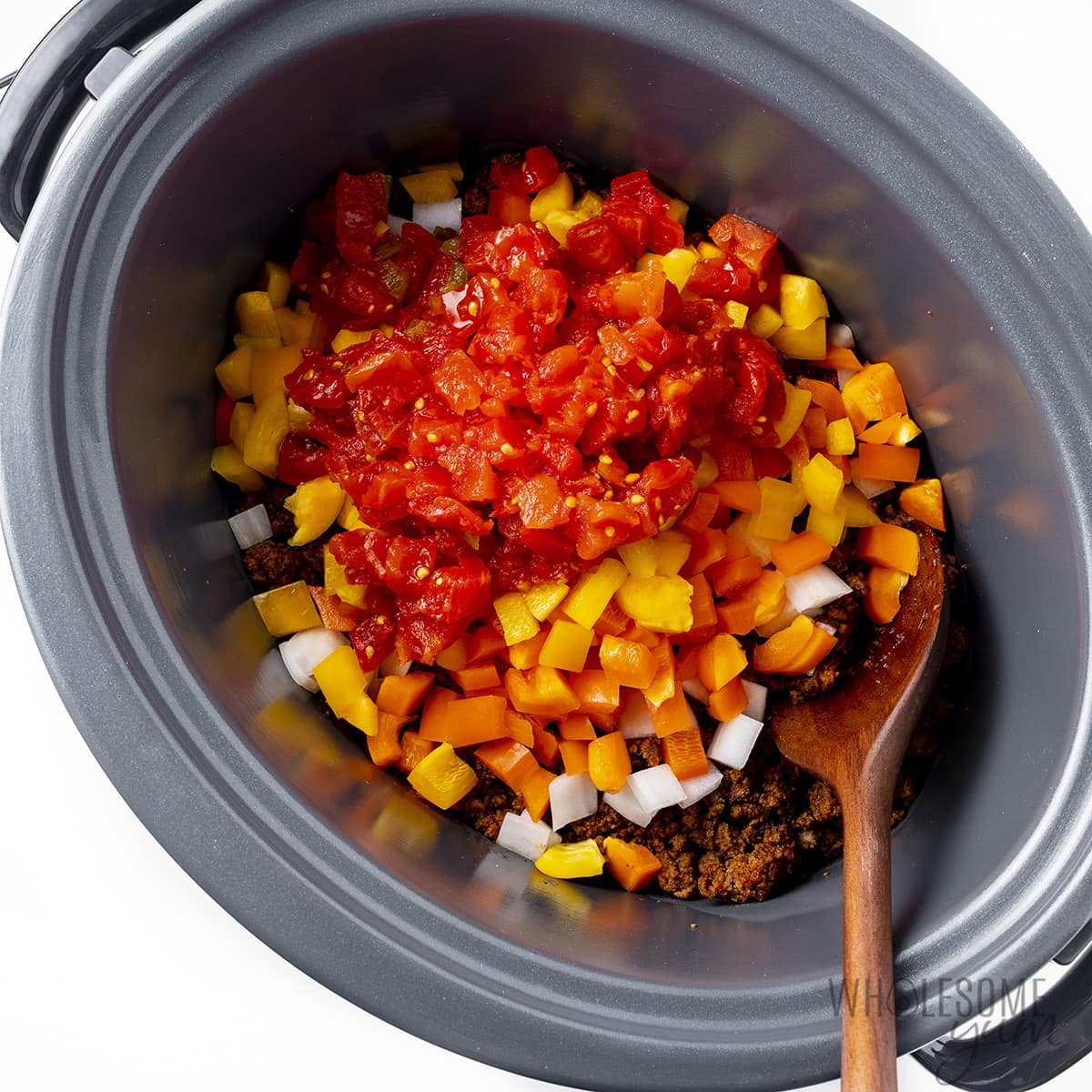 Mezcla de carne molida colocada en una olla de cocción lenta con pimientos, cebollas y tomates.