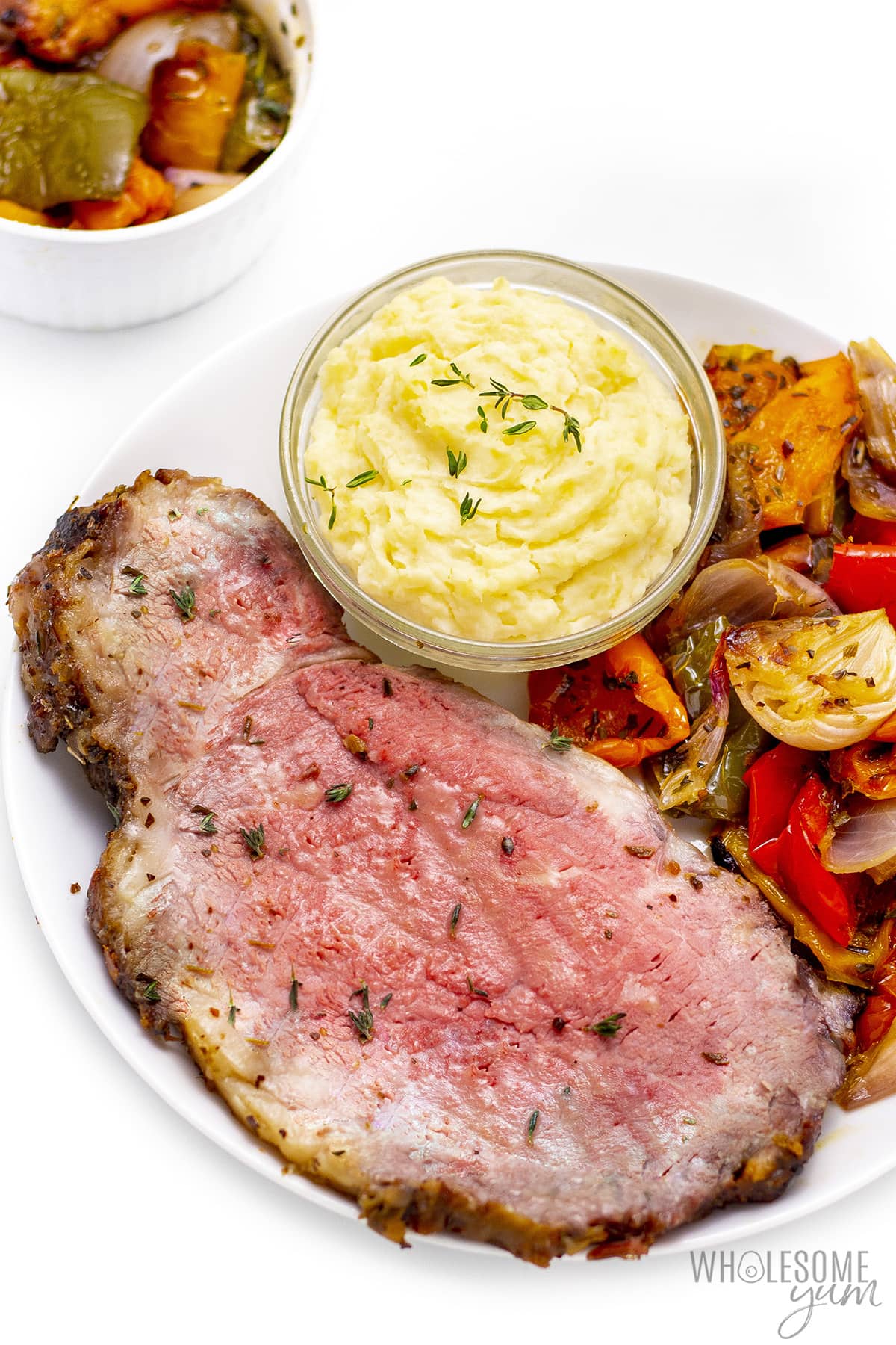 Prime rib on a plate next to veggies and horseradish sauce. 