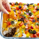 Taco dip recipe dunked with a hand holding a sliced bell pepper.
