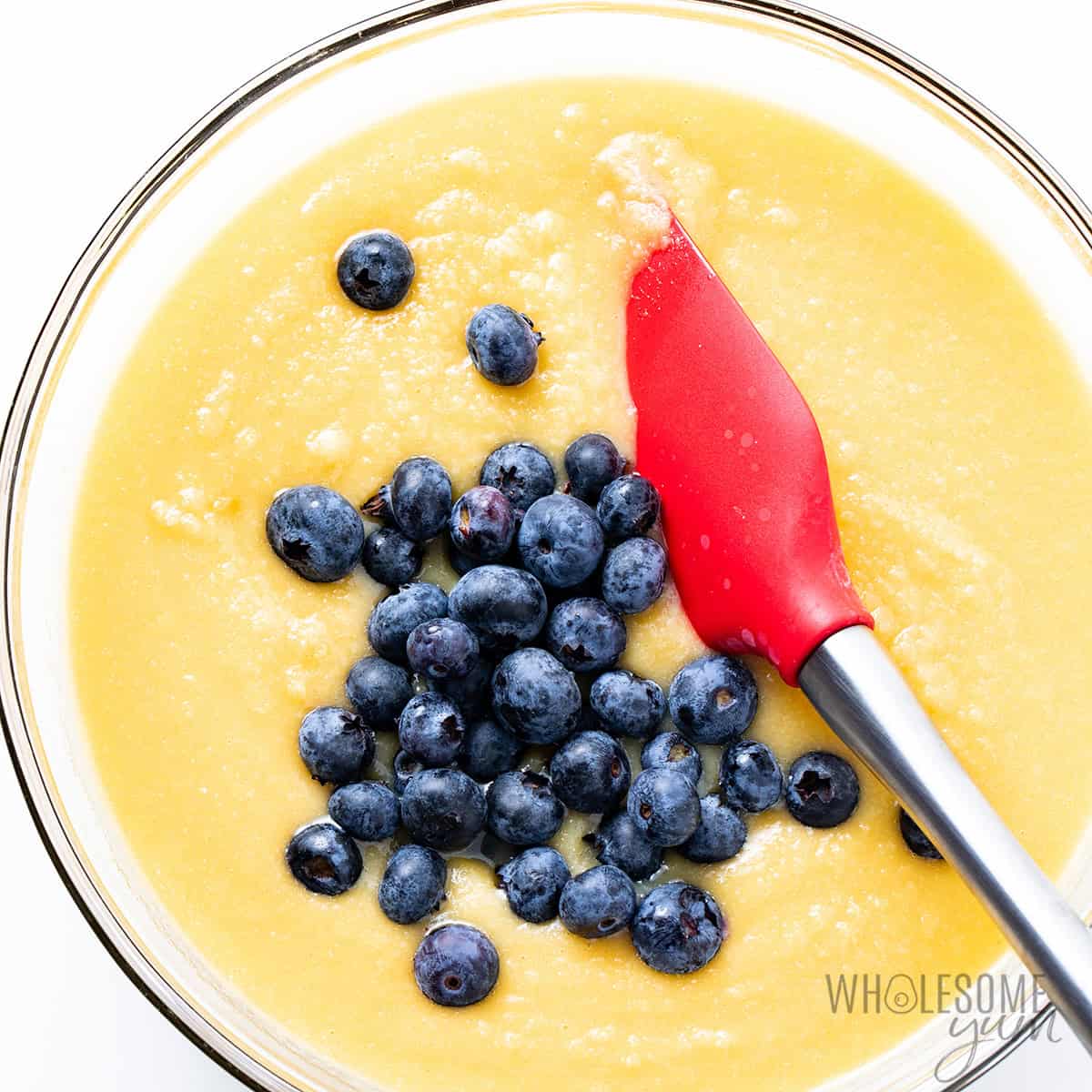Batter in a bowl with blueberries added and a spatula.