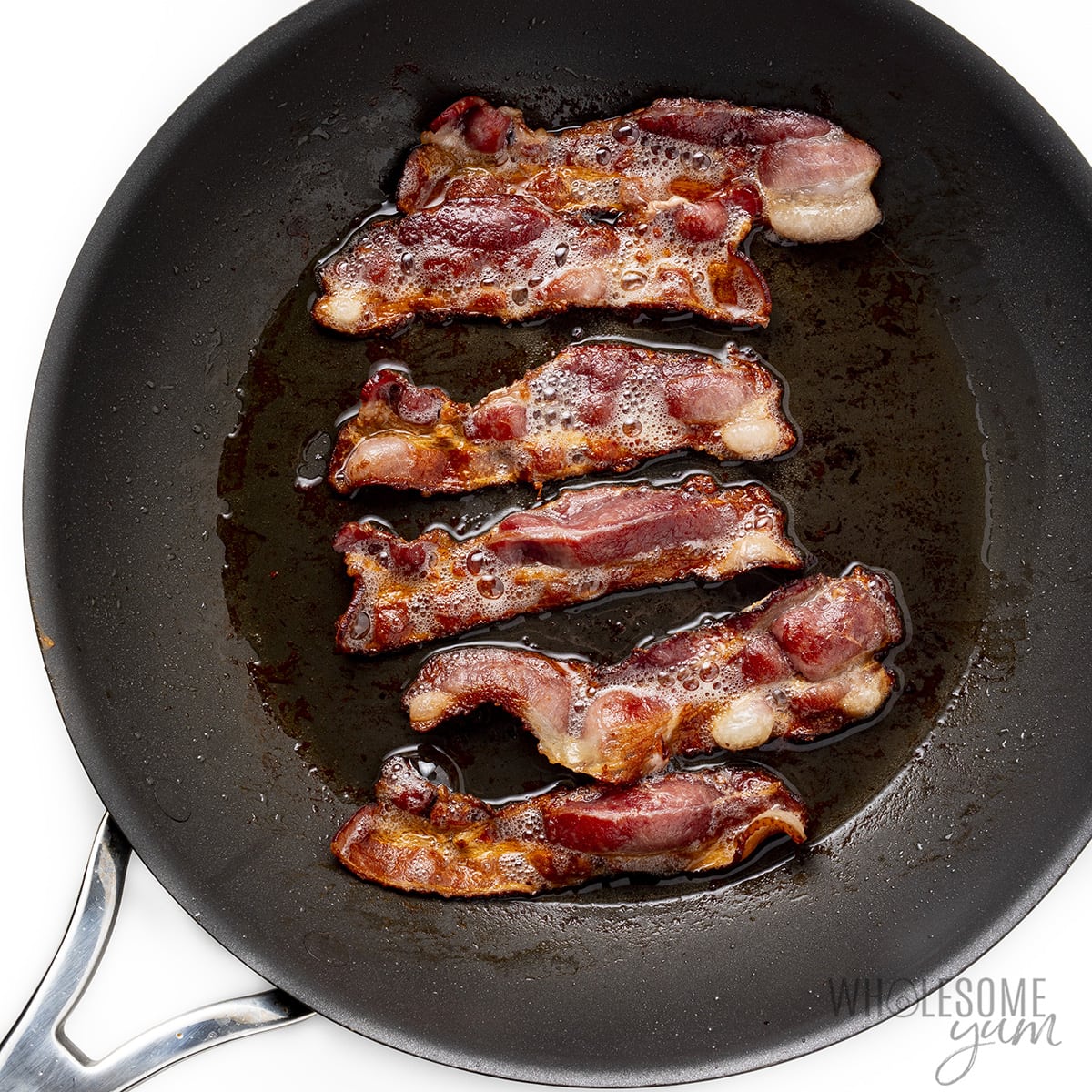 Bacon slices cooking in a skillet.