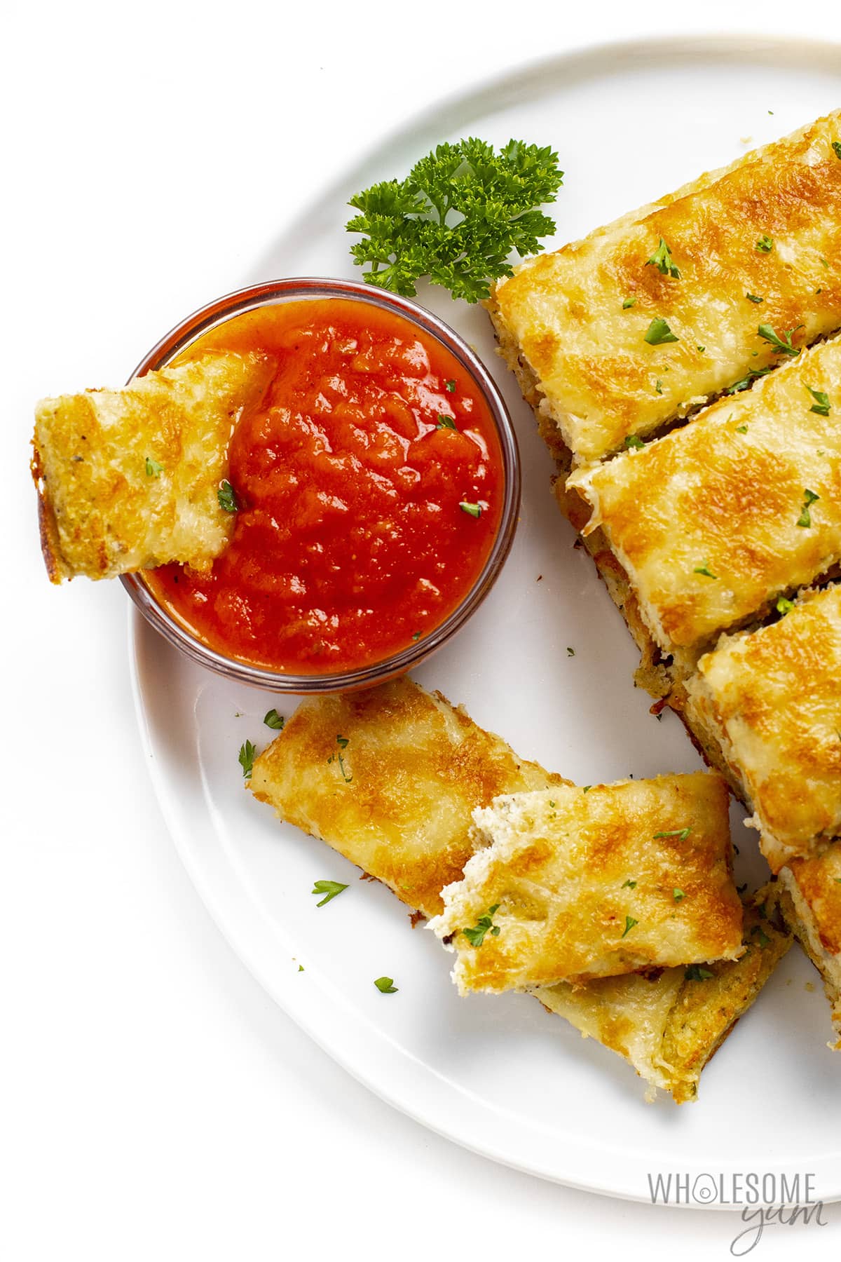Cauliflower breadsticks on a plate with one dipped in marinara.