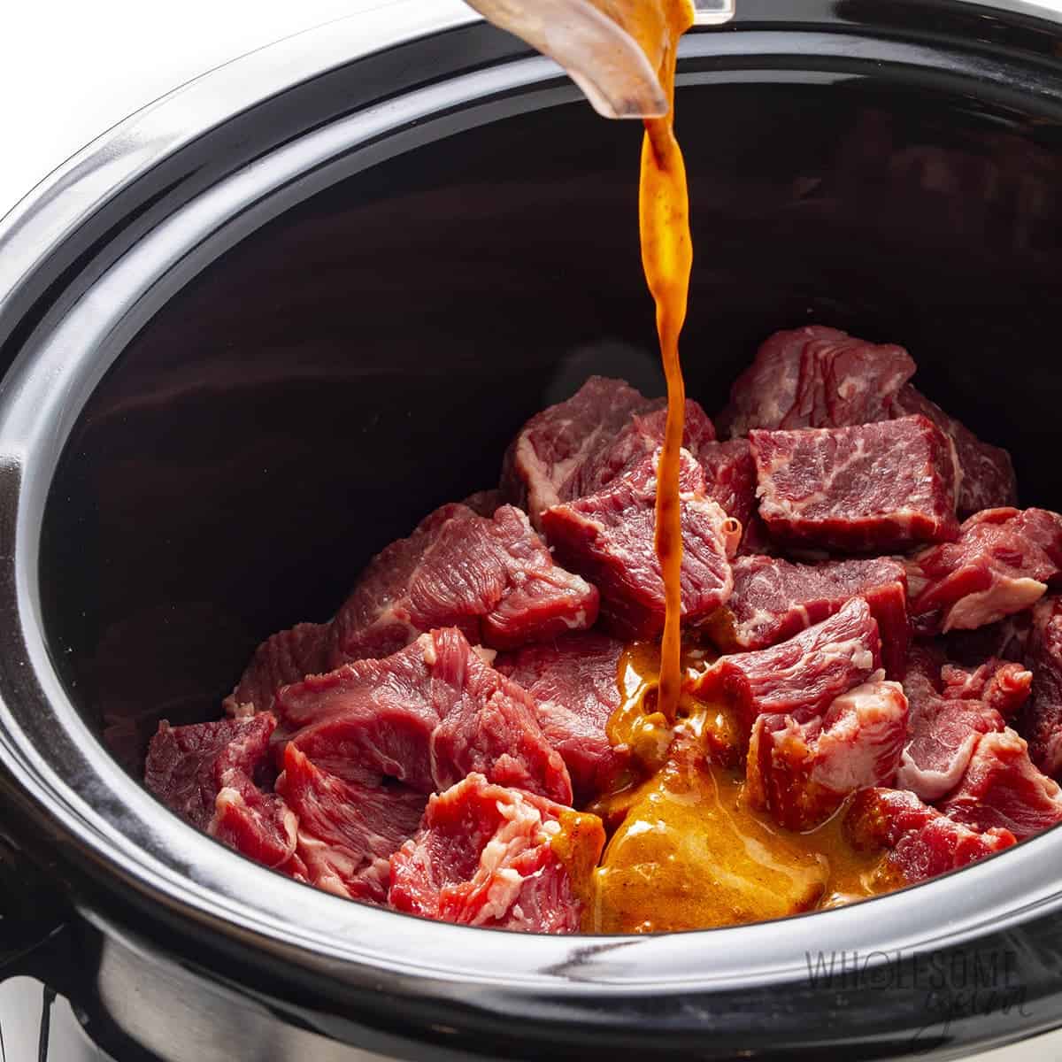 Pouring barbacoa seasoning sauce over beef in slow cooker.