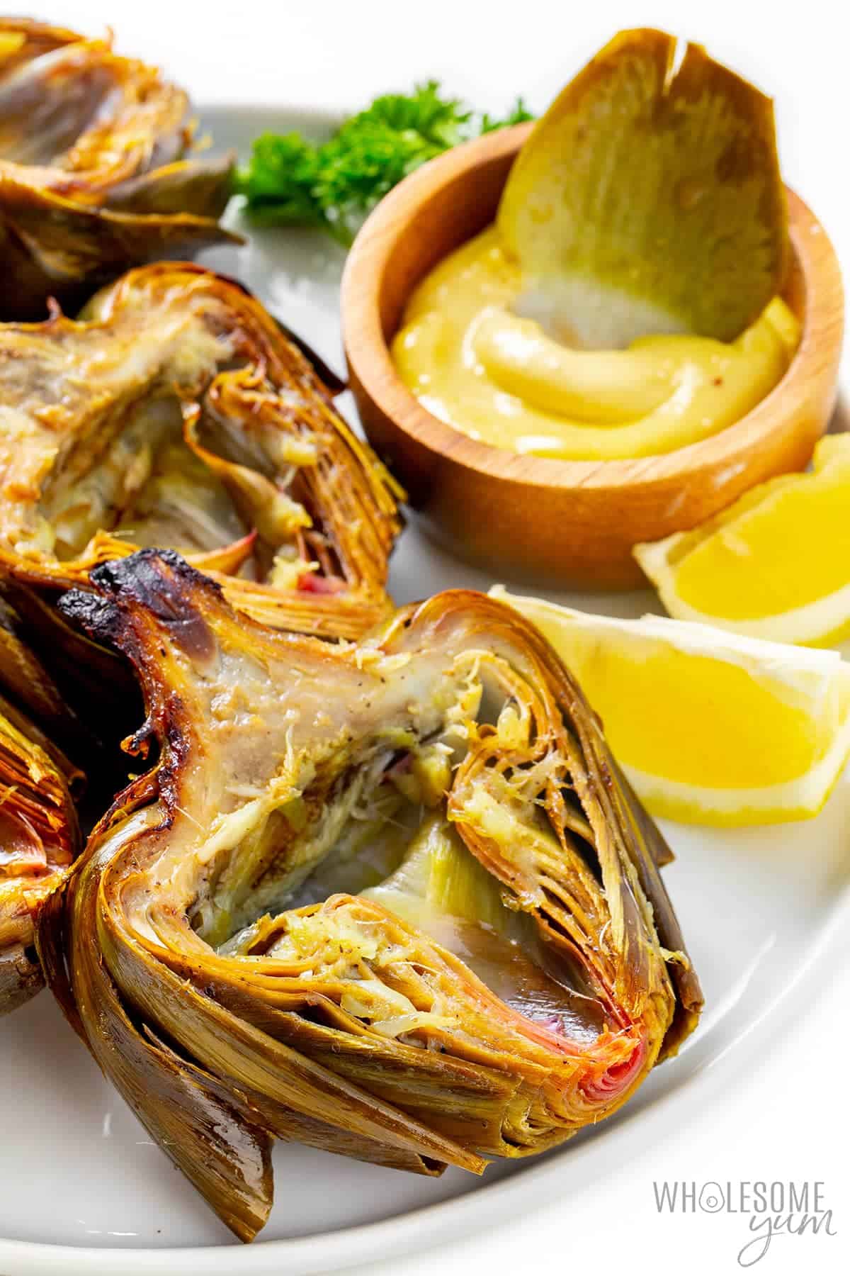 Finished artichokes on a plate with one petal dunked in aioli sauce.