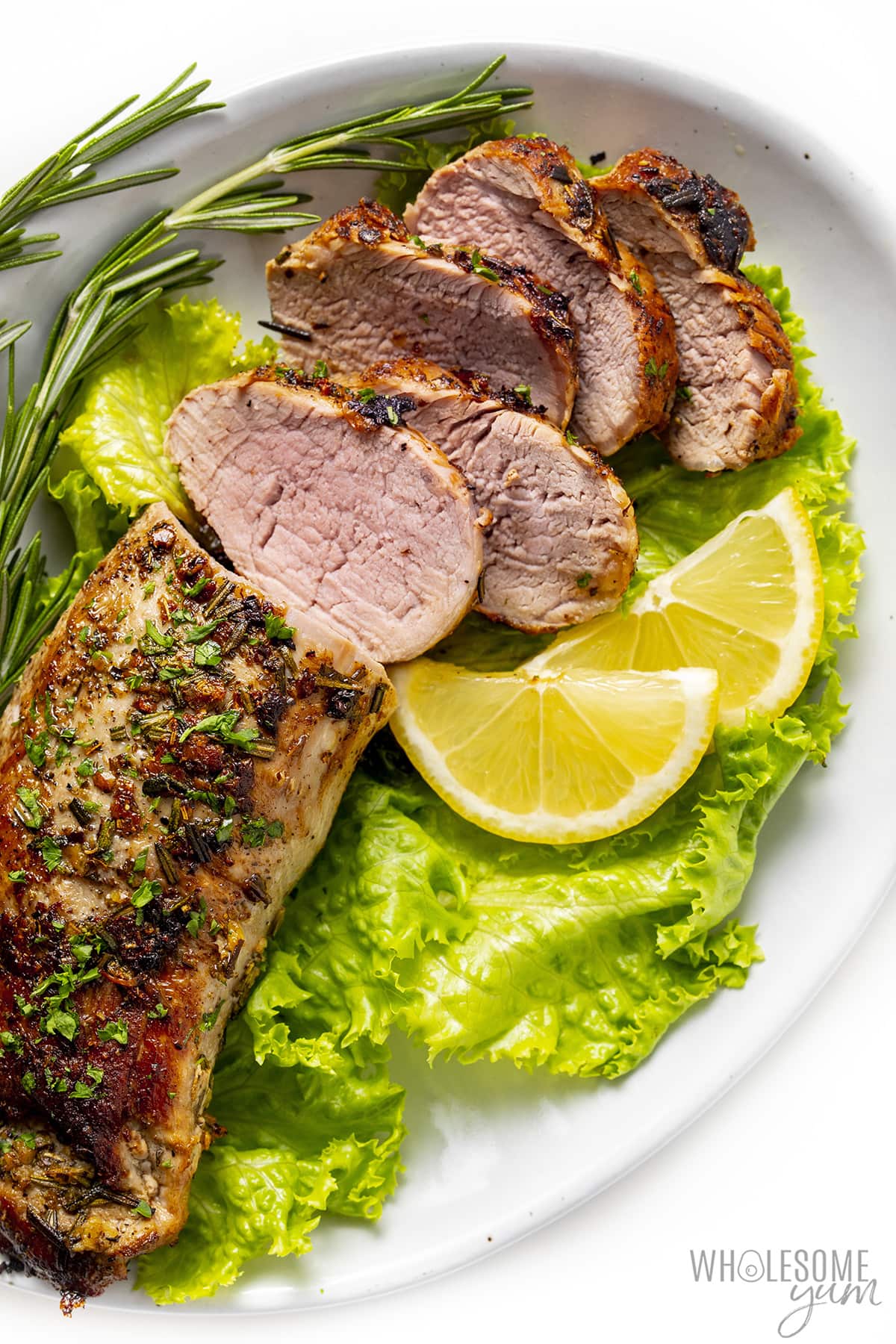 Pork tenderloin on a plate with lettuce and lemon slices. 