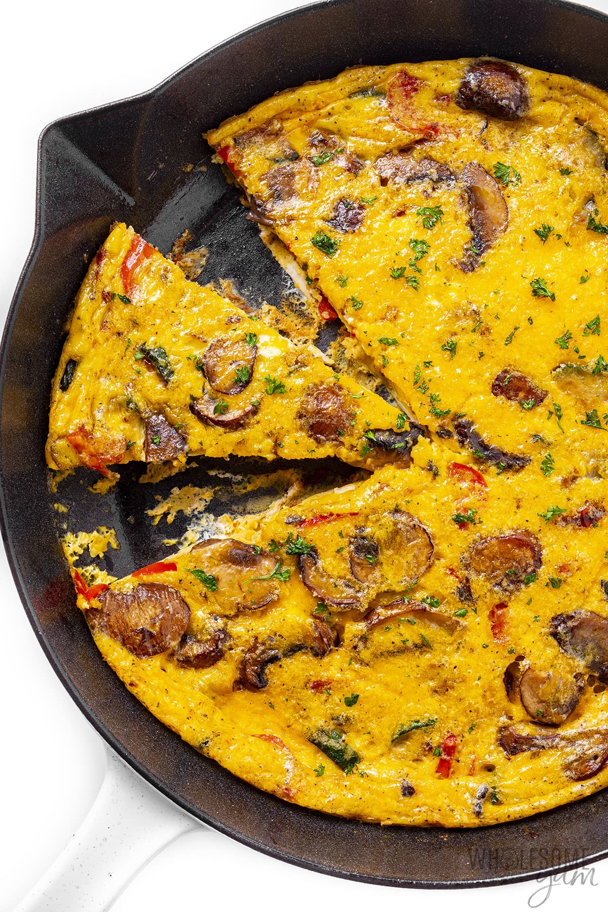 Vegetable frittata cut into slices in skillet.