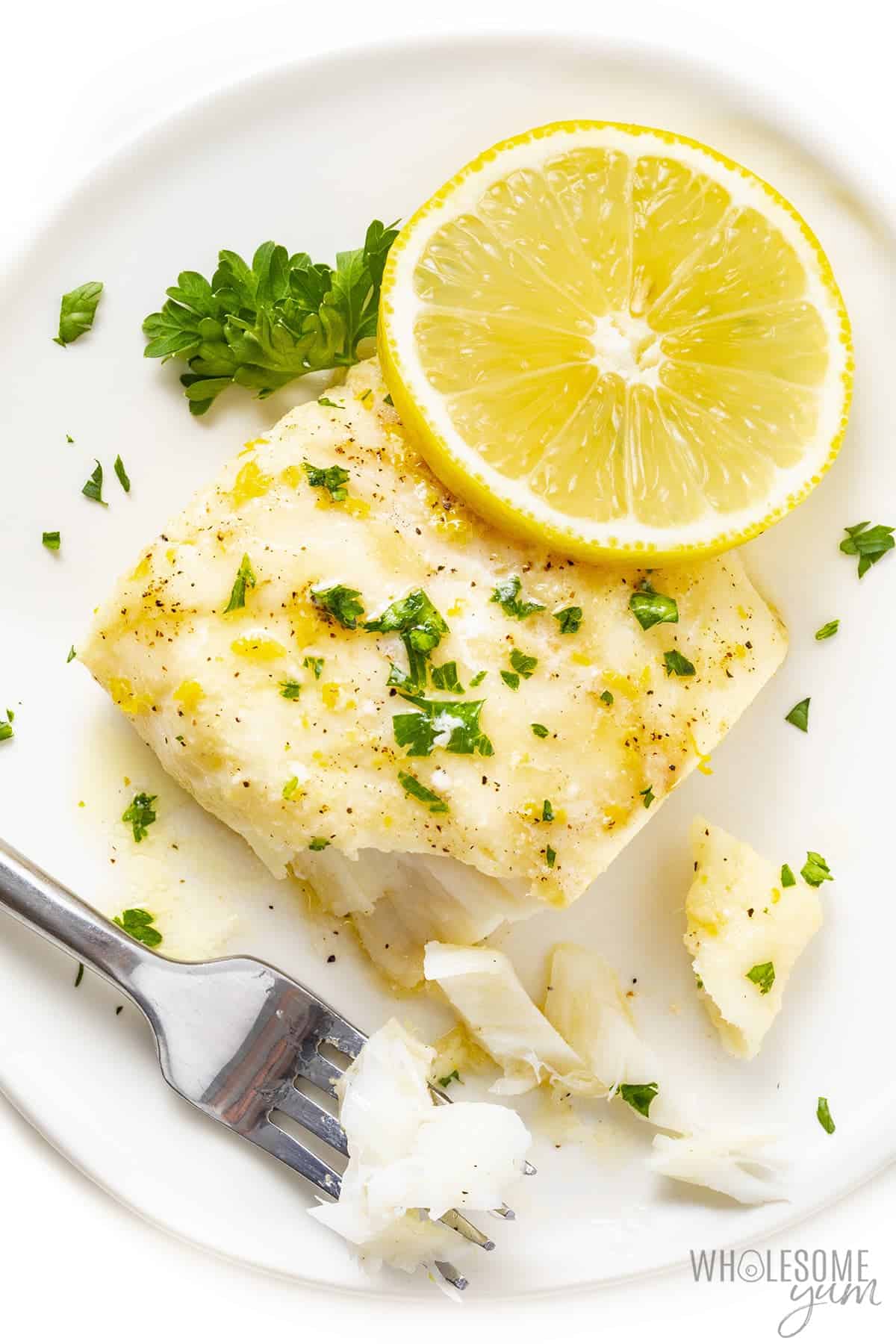 Baked cod recipe on a plate with fork and lemon slice