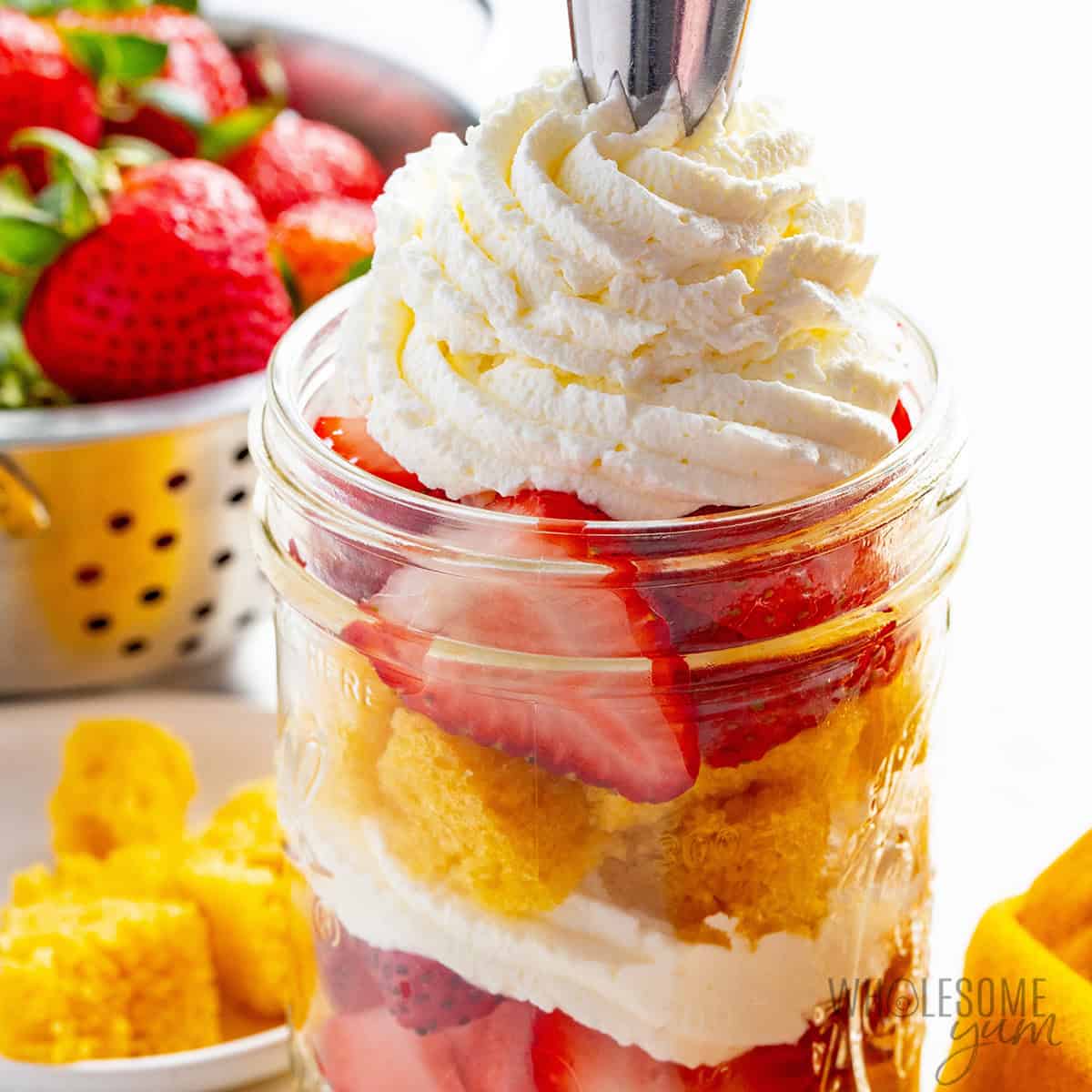 Topping strawberry shortcake in a jar with whipped cream.