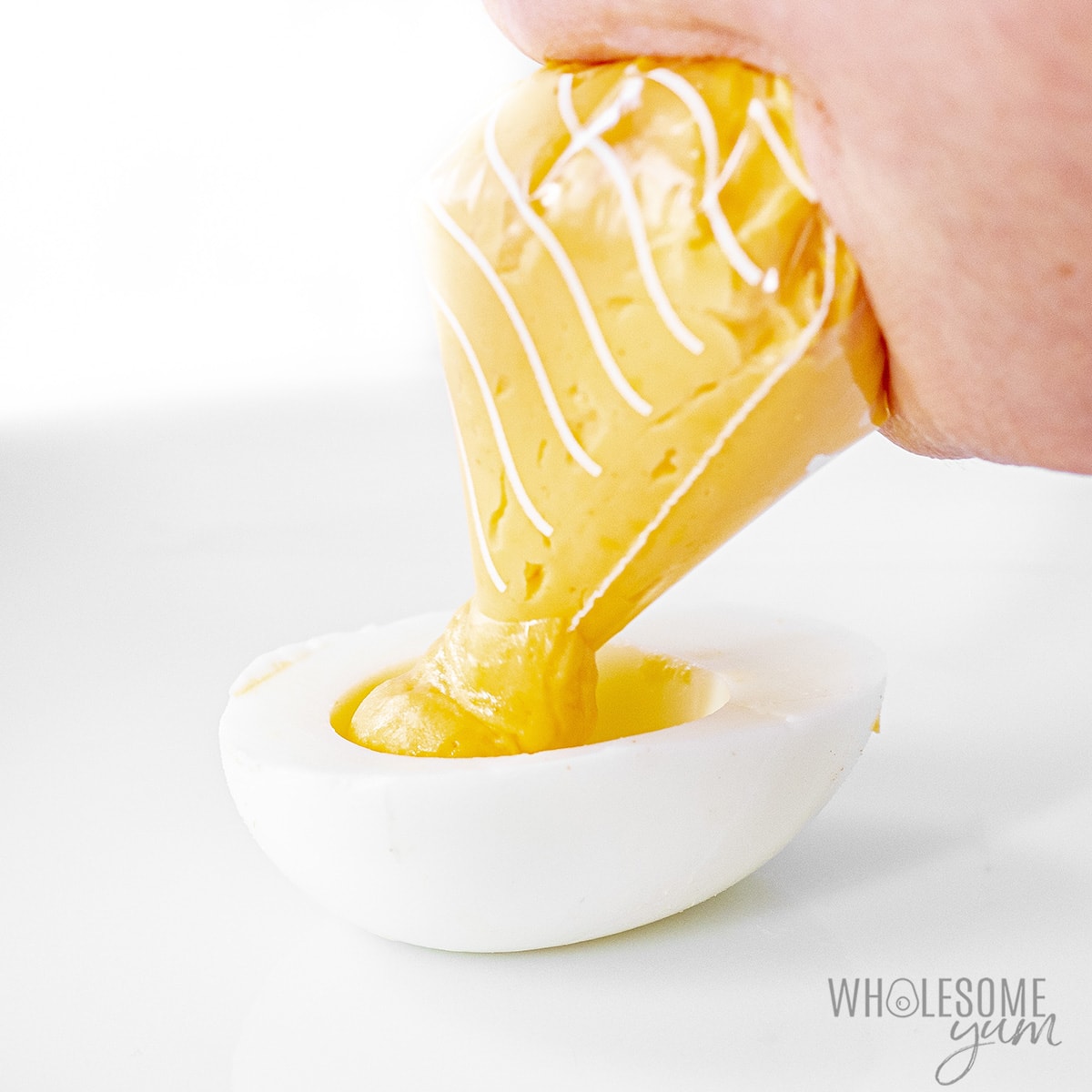 Yolk mixture in a piping bag being piped into sliced egg white.