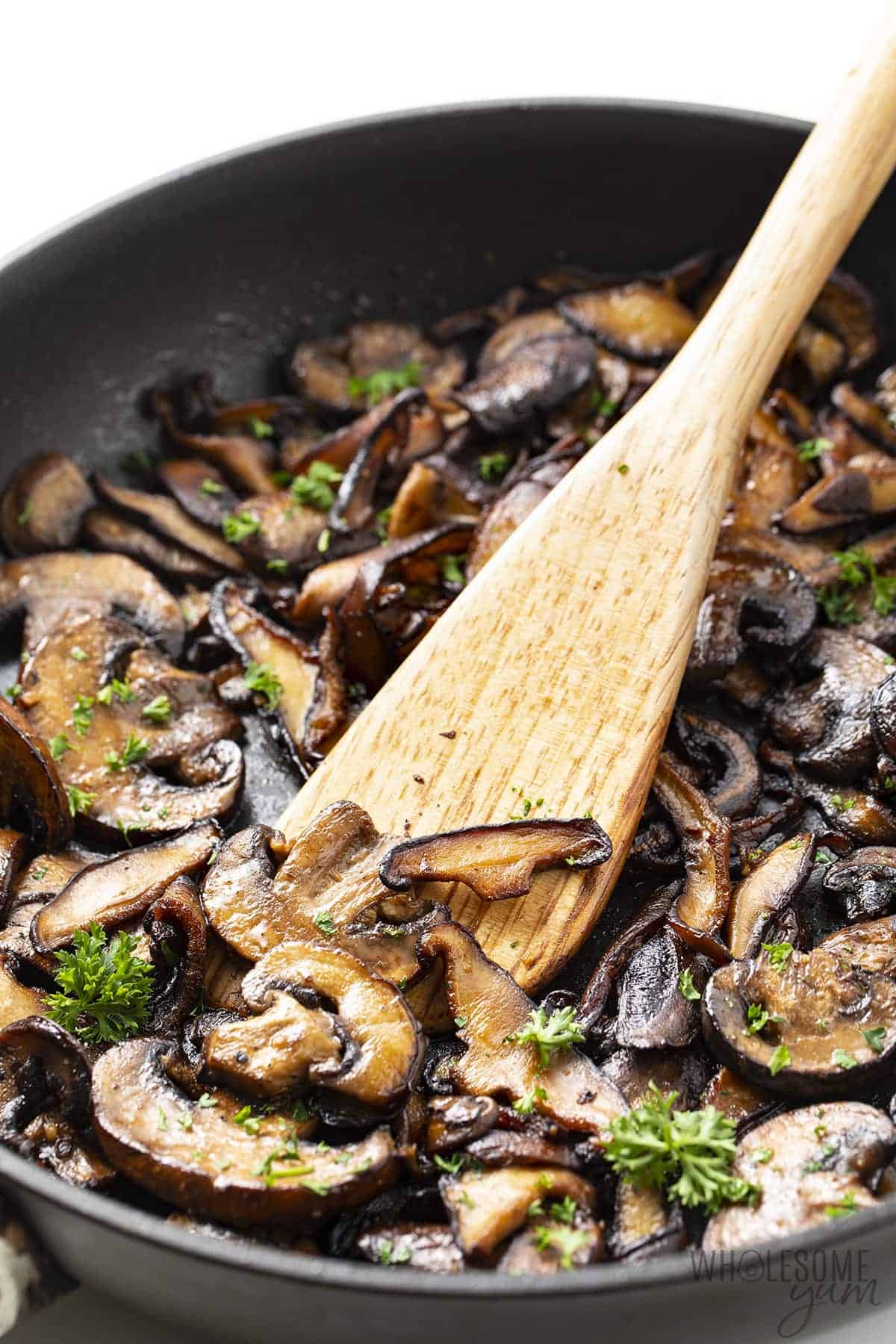 Garlic butter mushrooms in a skillet with wooden spatula.