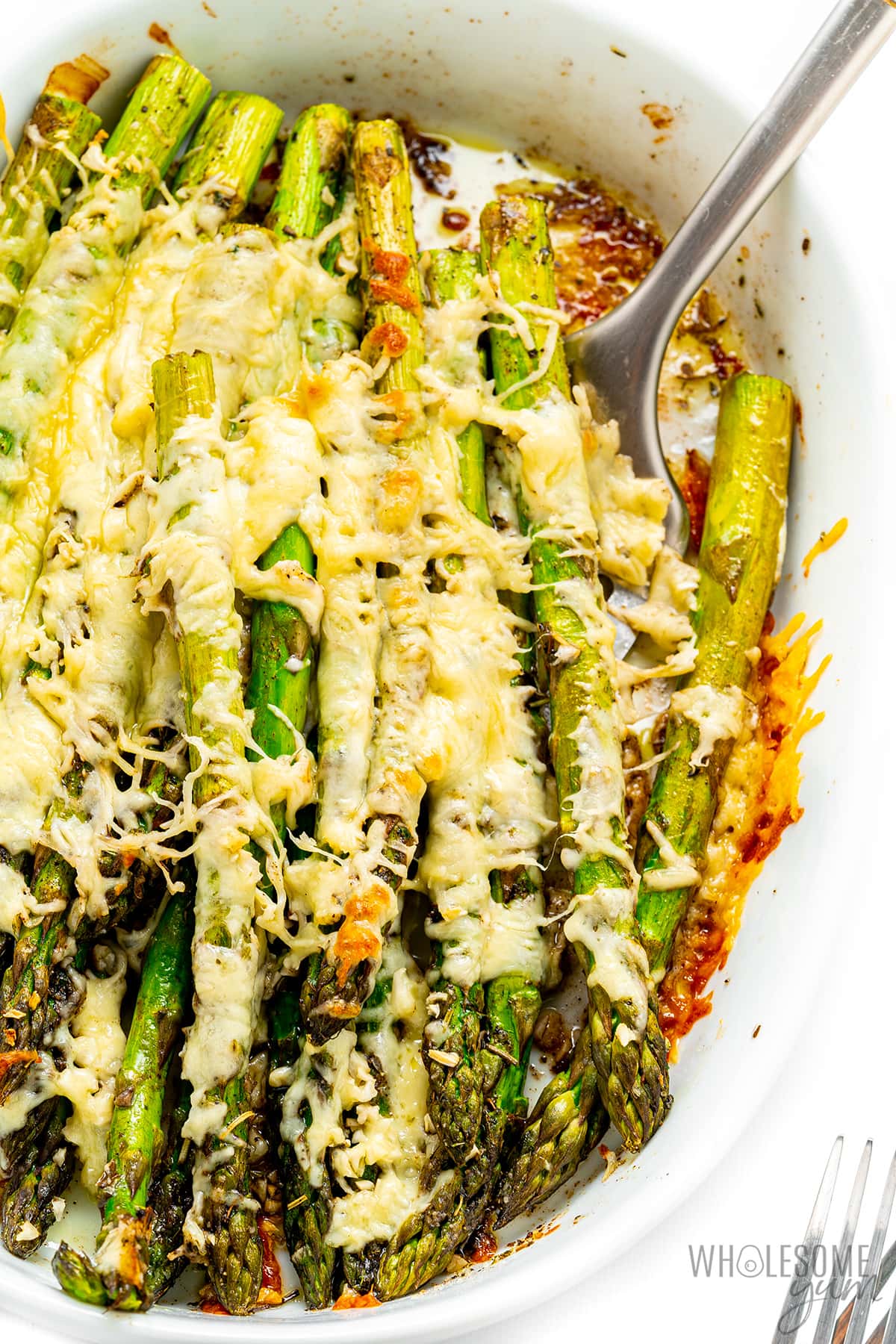 Cheesy asparagus in a casserole dish with a spatula.