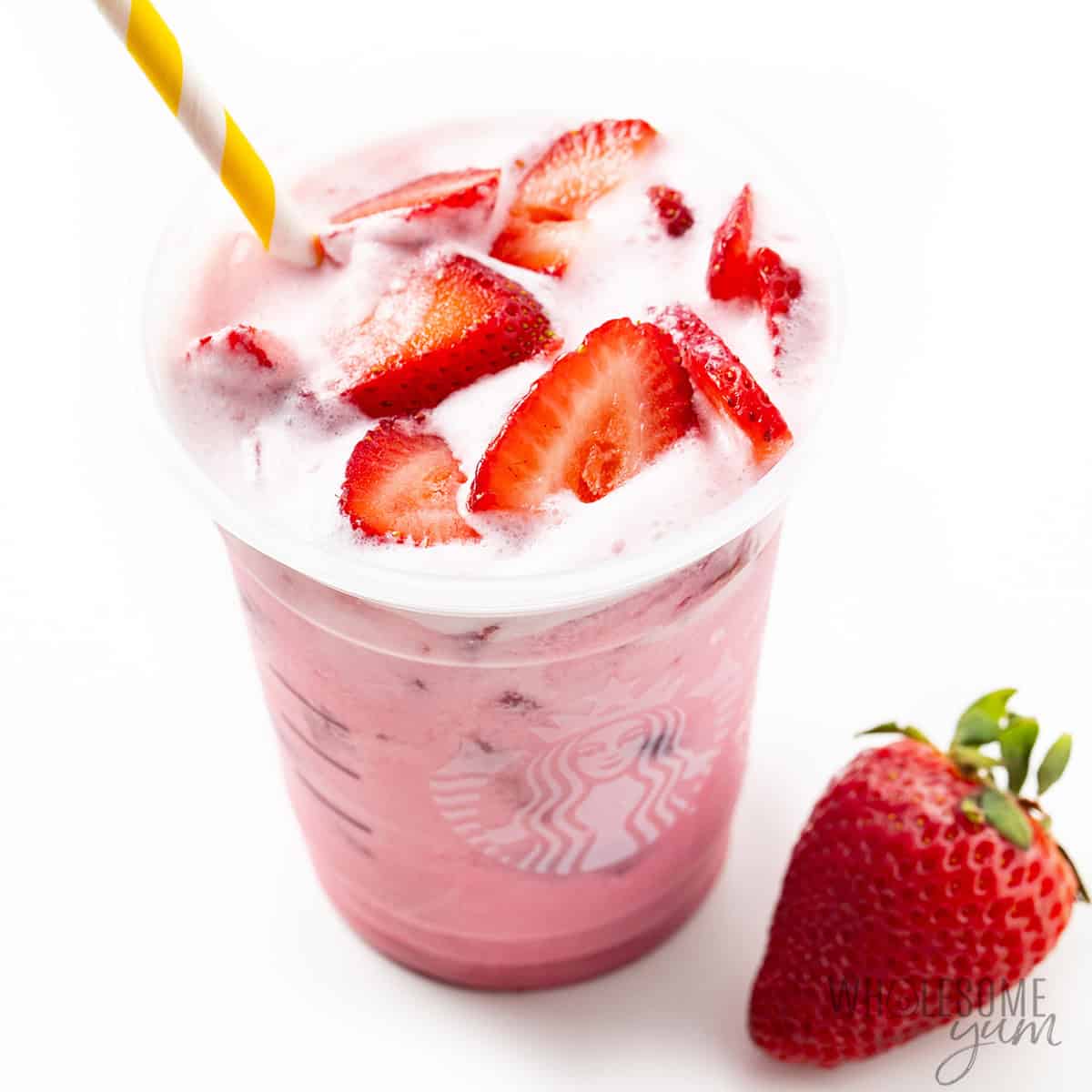 Assembled pink drink recipe, topped with sliced strawberries and a striped straw.