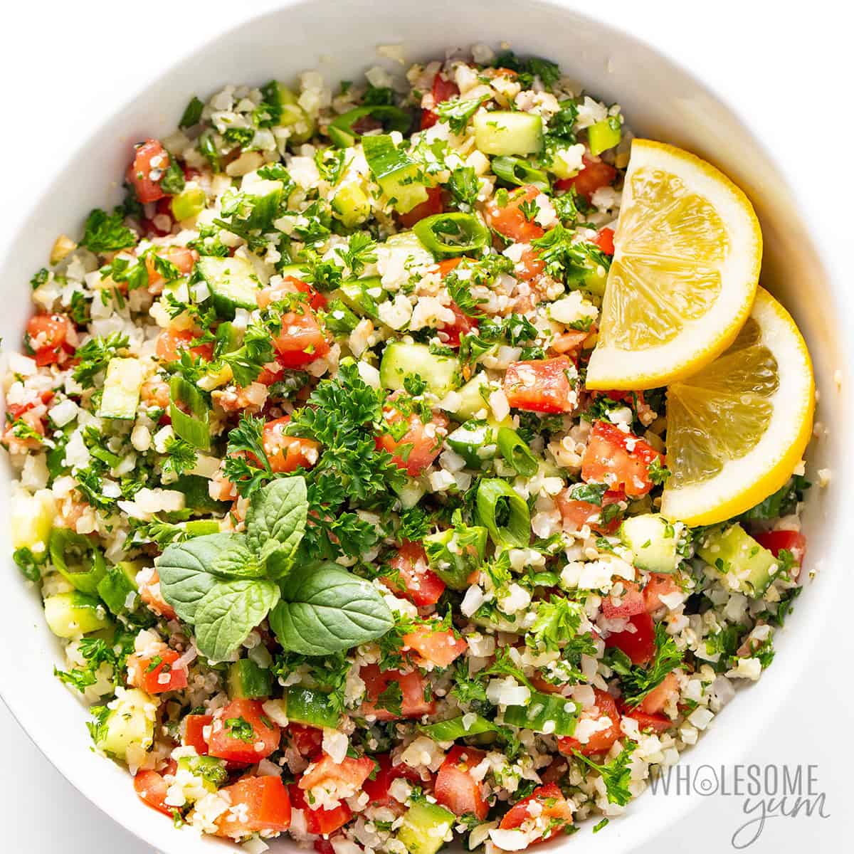Finished cauliflower tabbouleh recipe tossed in a bowl, garnished with lemon slices and mint.