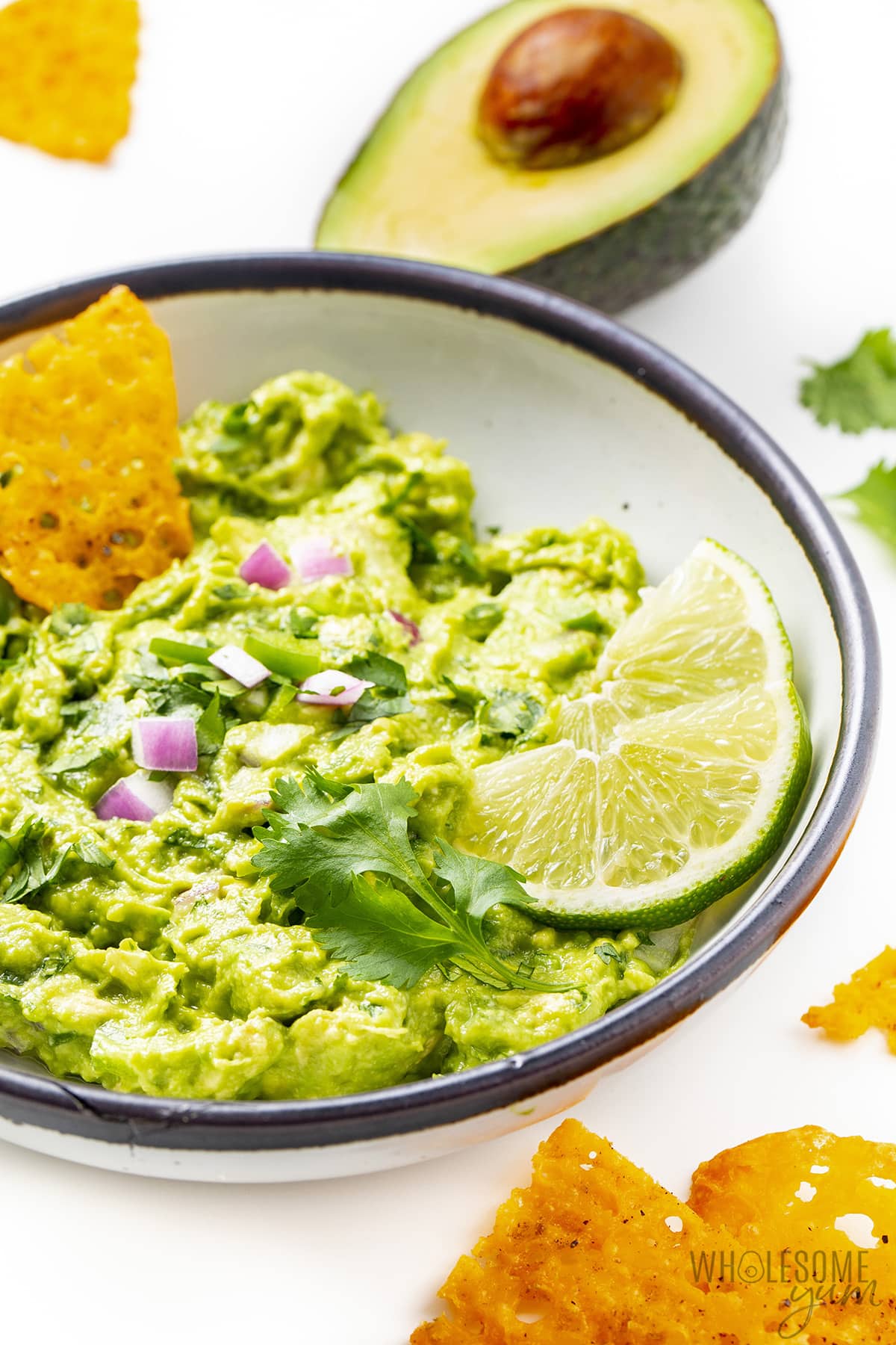 Best guacamole recipe in a bowl with a chip and lime wedges.