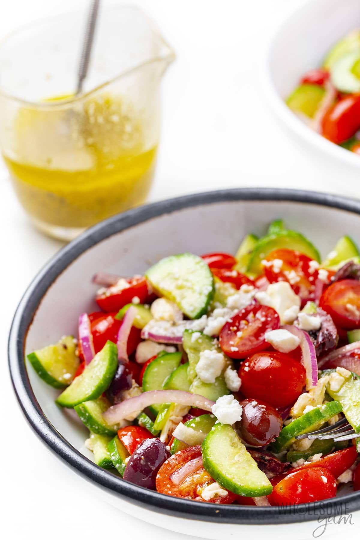 Traditional Greek salad (horiatiki salad) in a bowl with dressing in background.