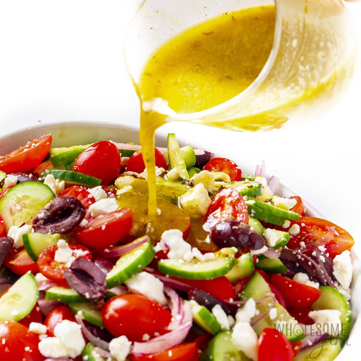 Dressing poured on Greek salad in a bowl.
