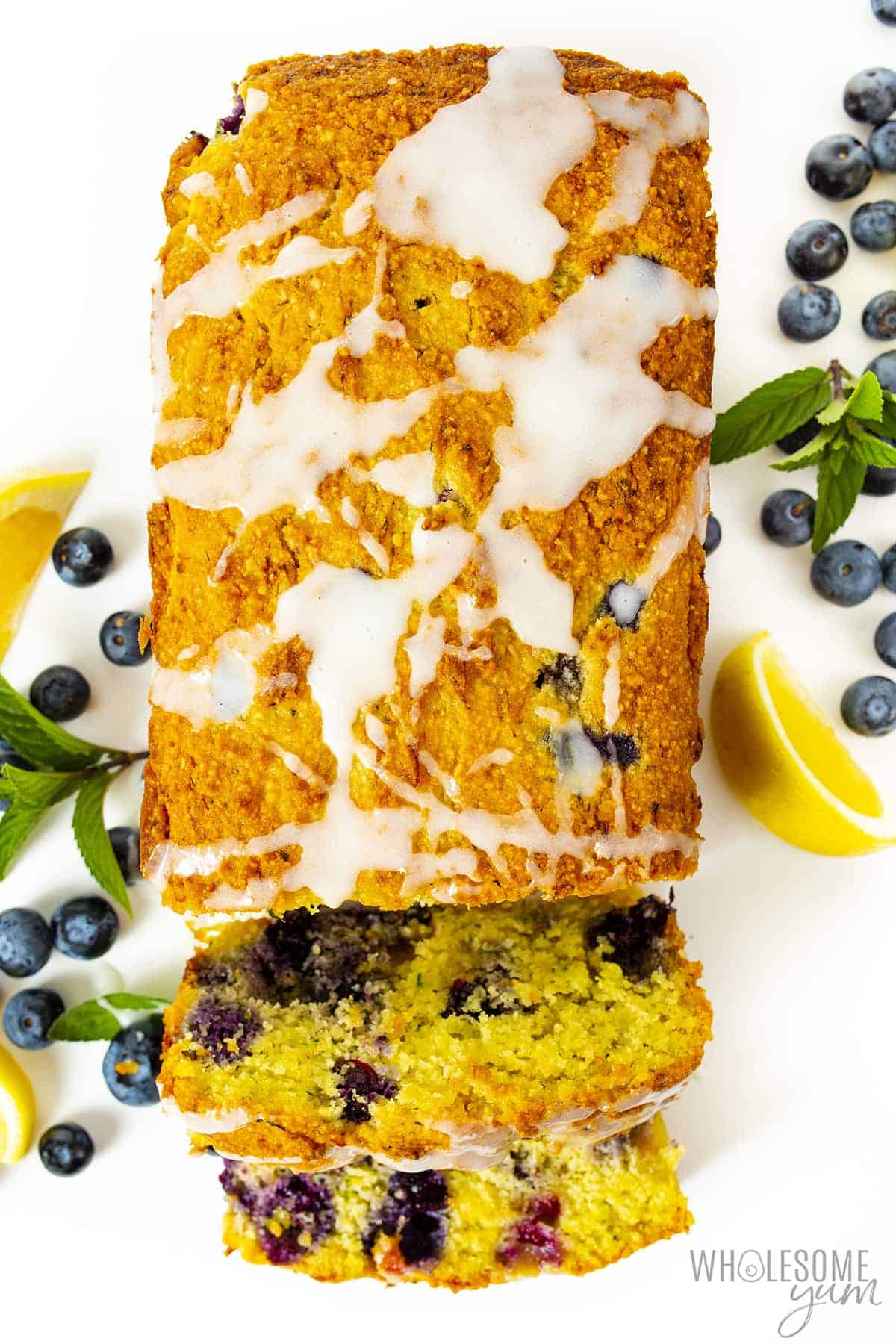 Blueberry keto zucchini bread loaf with a few slices cut, fresh blueberries, and lemon wedges.
