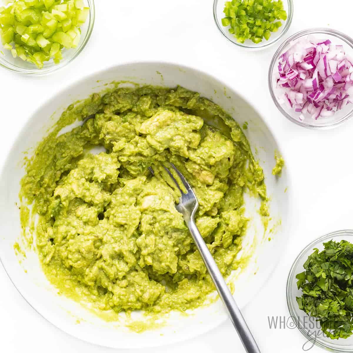 Mashed avocado with other salad ingredients to the side.