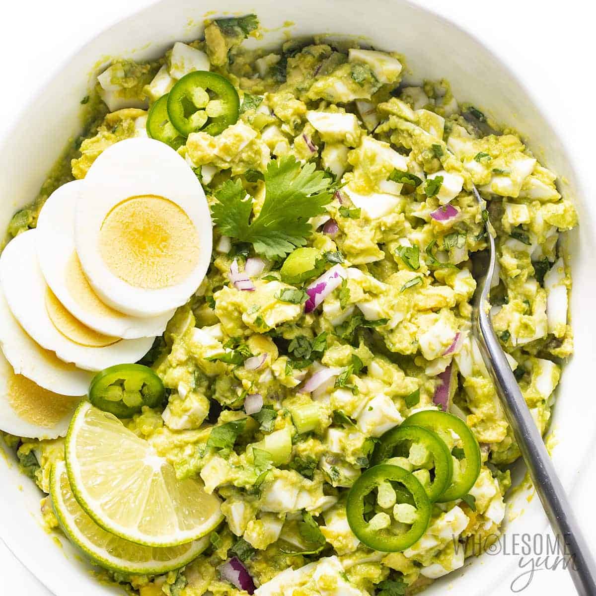 Avocado egg salad without mayo in a bowl with garnishes.