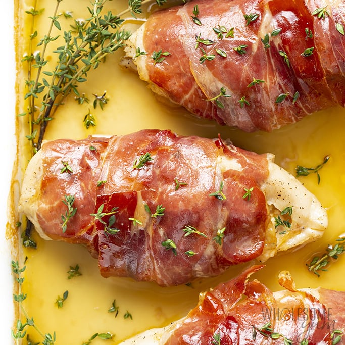 overhead view of prosciutto wrapped chicken in a baking dish with thyme as garnish