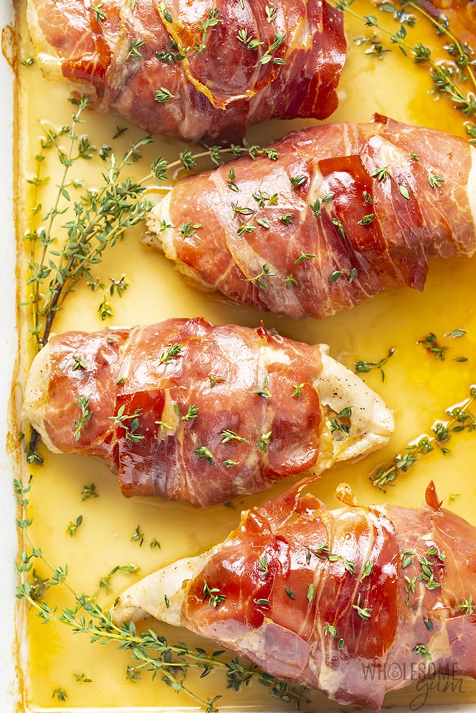 Overhead view of prosciutto wrapped chicken in a baking dish with thyme as garnish