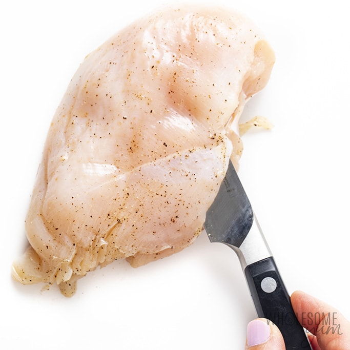 Chicken breast being sliced in half so that it can be stuffed