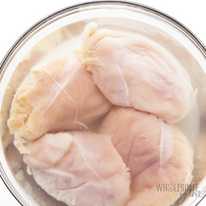 Overhead shot of chicken breast in a bowl of brining liquid