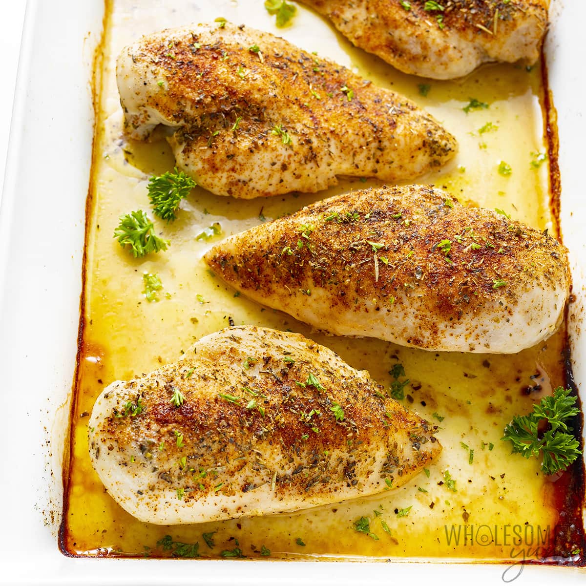 Oven baked chicken breasts in baking dish.