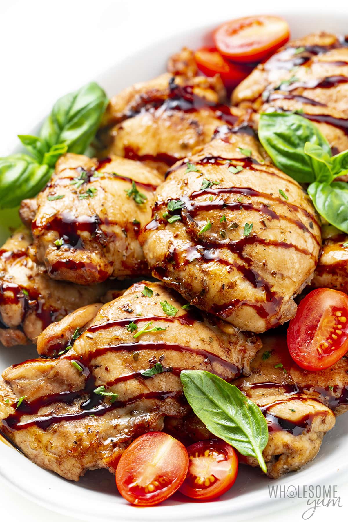 Balsamic glazed chicken on a serving plater with basil leaves and tomatoes.