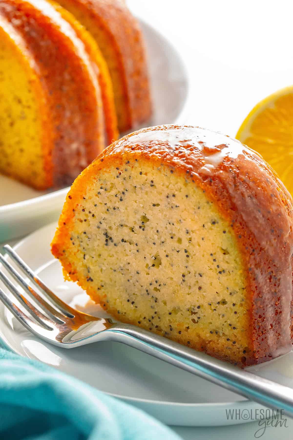 Slice of lemon poppy seed bundt cake on a plate, drizzled with a tangy lemon glaze.