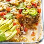 Overhead view of Mexican ground beef casserole in a casserole dish divided into 9 servings with cilantro, jalapenos, and avocado slices and a slice removed
