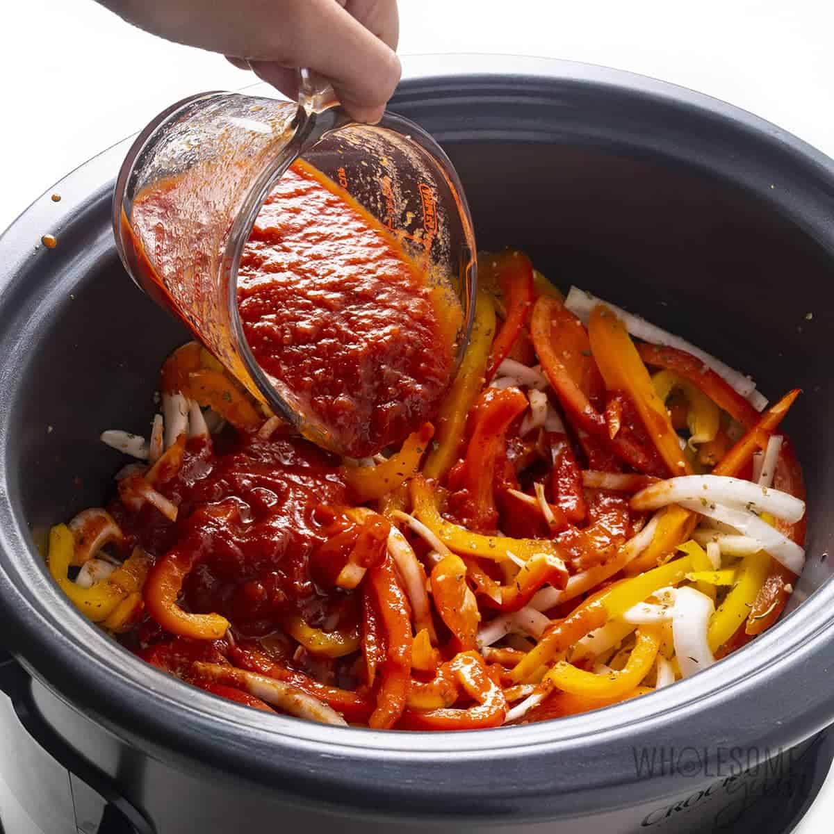 Marinara being poured over the sausage and peppers recipe in slow cooker.