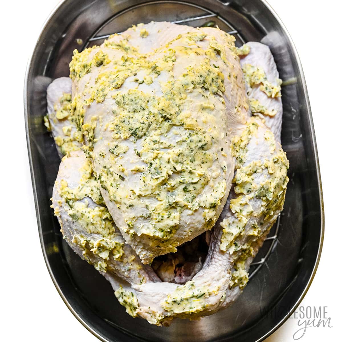 Turkey covered in butter mixture in roasting pan.
