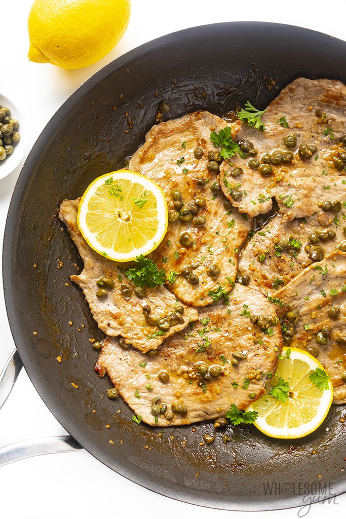 Veal piccata in a skillet topped with capers and lemon slices