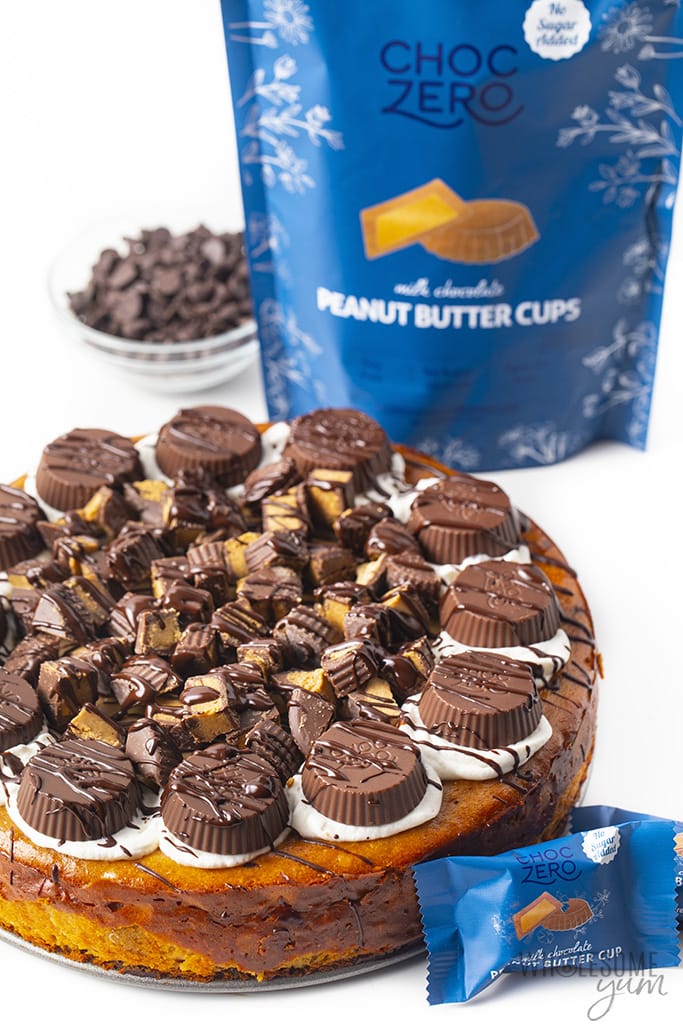 Side view of a whole peanut butter cup cheesecake with a bag of peanut butter cups
