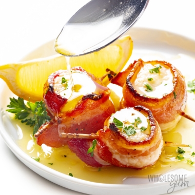 Bacon wrapped scallops drizzled with lemon butter sauce on a plate.