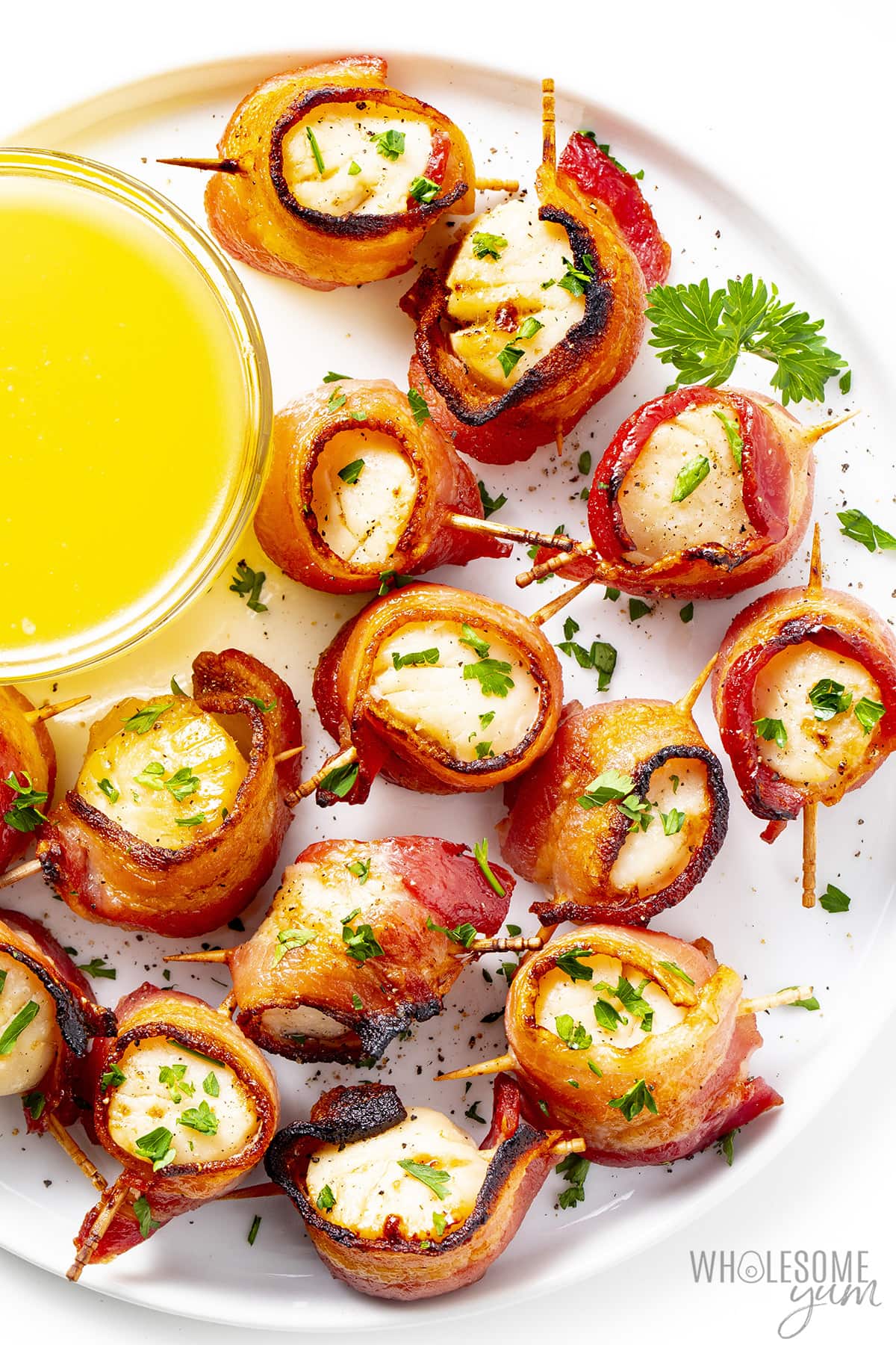 Bacon wrapped scallops piled together on a plate and sprinkled with parsley.