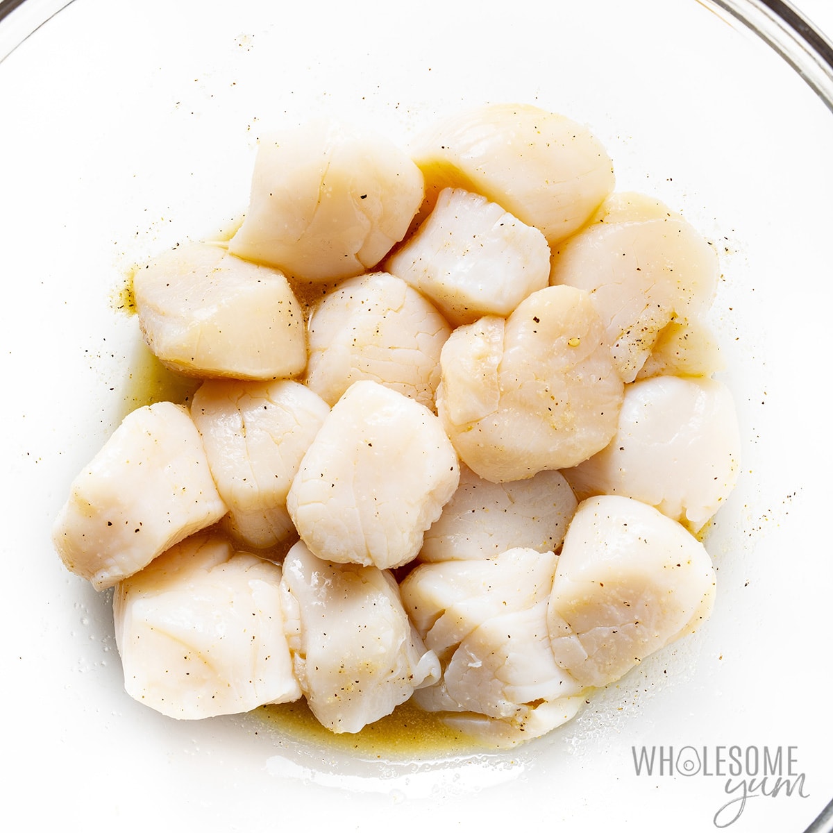 Raw scallops in a bowl, seasoned with salt and pepper.
