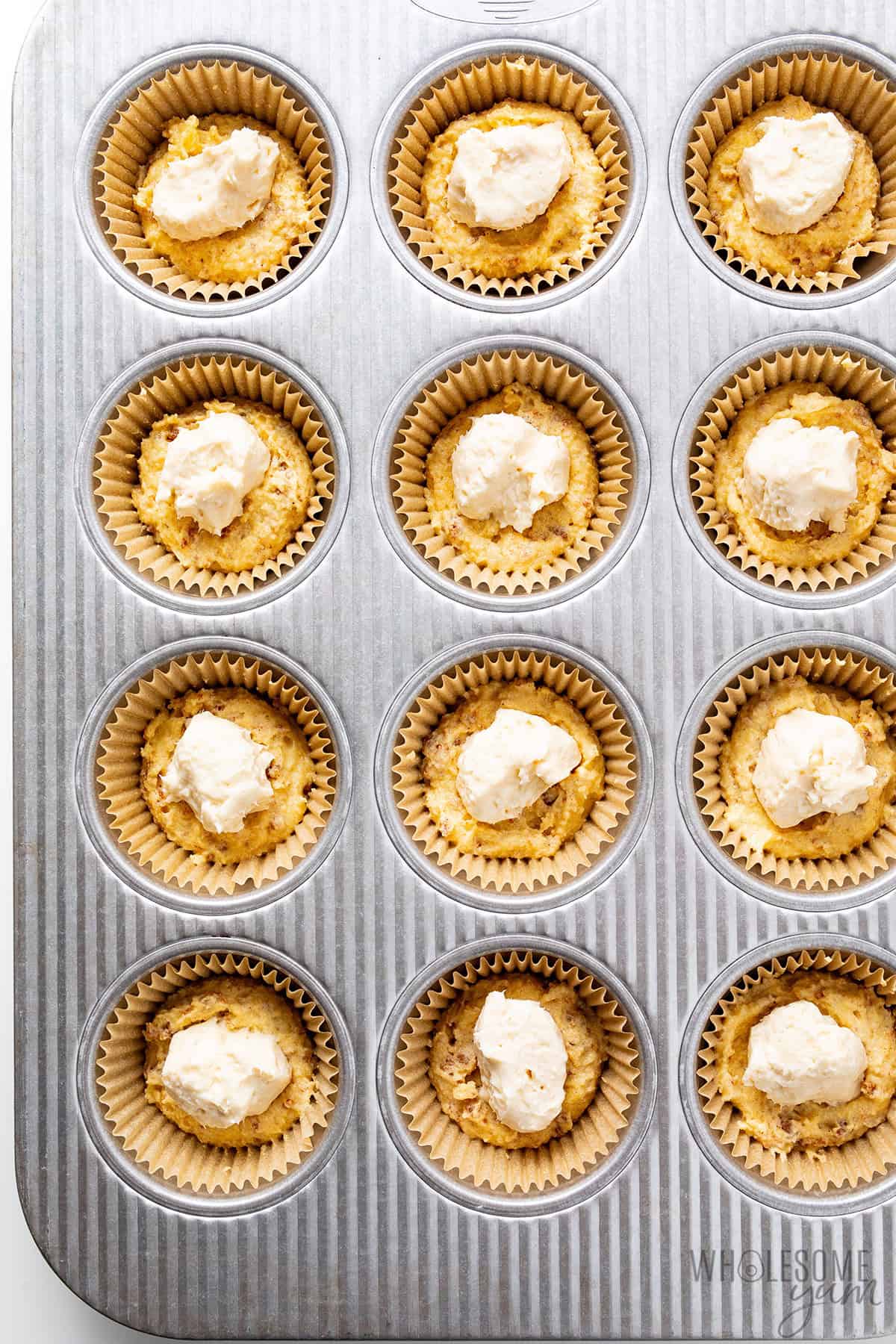 Muffin batter divided among lined muffin cups with cream cheese filling added in the center of each.