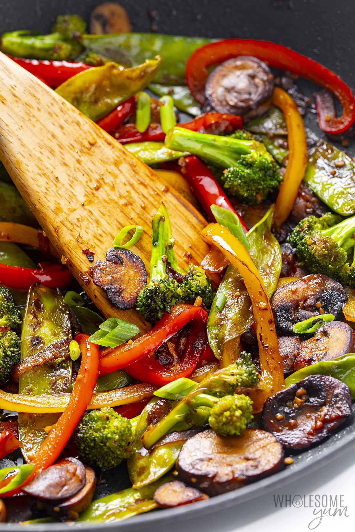Stir fry vegetables in a wok with a wooden spoon.