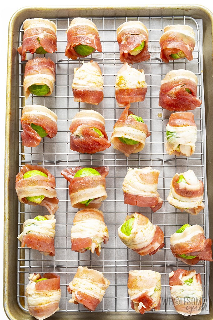 Brussels sprouts wrapped in bacon on a baking sheet with a rack