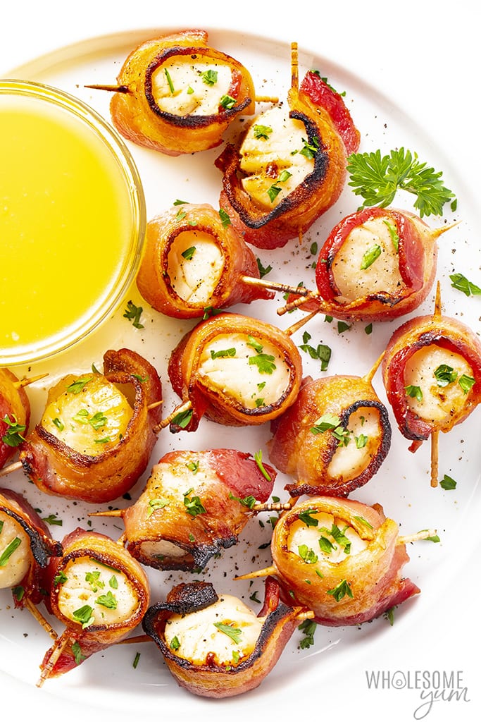 Bacon wrapped scallops on a serving plate with lemon butter sauce