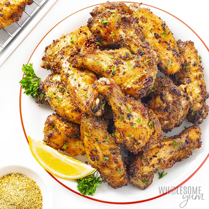 Lemon pepper wings stacked on a white plate with a lemon wedge